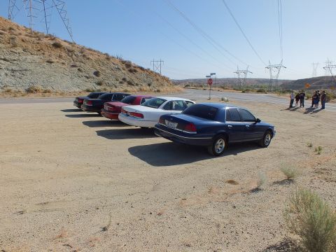 2003 Ford Crown Victoria - dark blue Crown Victoria heads a lineup of sedans on a dirt lot under transmission towers