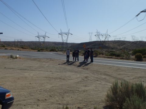 2003 Ford Crown Victoria - Several people stand beside a paved desert road as power pylons stretch across the dry hills