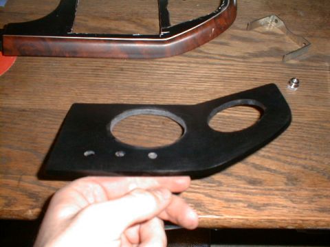 1990 Ford Bronco - A hand holds a black plastic part with openings, possibly for gauges, on a wooden surface.