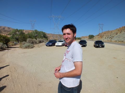 2003 Ford Crown Victoria - Man poses on a sandy lot; five sedans and tall power-line towers fill the desert background.