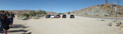 2003 Ford Crown Victoria - Wide view of a roadside lot: people gather at left while five cars park beneath power lines.