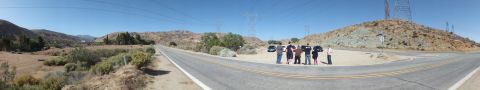 2003 Ford Crown Victoria - People line a dirt shoulder along an empty desert highway under transmission towers.