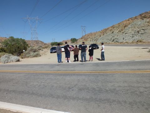 2003 Ford Crown Victoria - Six people stand together on a sandy pullout, cars and power towers behind them.