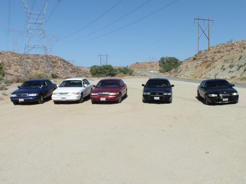 2003 Ford Crown Victoria - Front view of five parked sedans in blue, white, maroon and black under power towers.