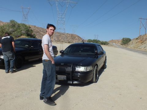 2003 Ford Crown Victoria - Man stands at the front of a blacked-out Crown Victoria with grille guard in the desert