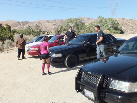 2003 Ford Crown Victoria - Owners gather among black and maroon full-size sedans at a dusty desert pullout