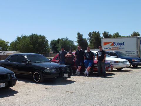2003 Ford Crown Victoria - Owners pose before a row of black and red sedans with a Budget box truck in back