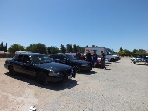 2003 Ford Crown Victoria - Black full-size sedans on a gravel lot as people gather near a Budget moving truck