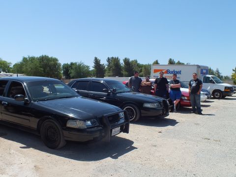 2003 Ford Crown Victoria - Row of blacked-out Crown Victoria Police Interceptors with people and a Budget box truck in the background.