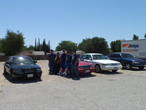 2003 Ford Crown Victoria - Attendees stand beside a red sedan in a lineup of full-size sedans and a Budget truck.