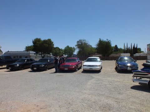 2003 Ford Crown Victoria - Sedan meet lineup in a gravel lot with a watercraft trailer parked at the right.