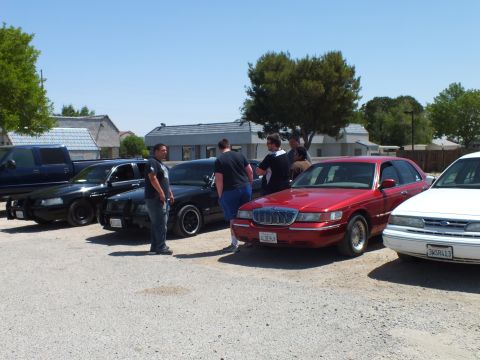 2003 Ford Crown Victoria - People stand around a red Grand Marquis flanked by black and white full-size sedans.