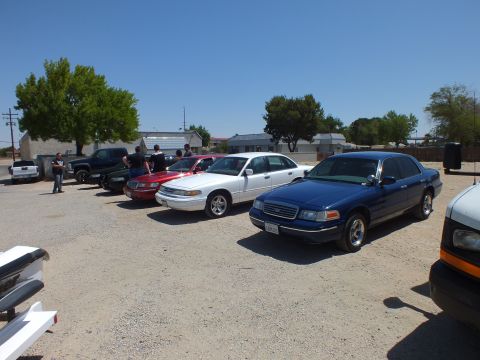 2003 Ford Crown Victoria - Dark blue Crown Victoria heads an angled lineup of sedans across a gravel lot.