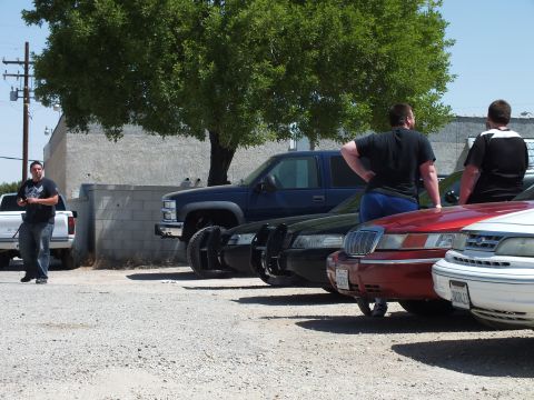 2003 Ford Crown Victoria - Attendees stand by a dark pickup behind the rear ends of red and white sedans.