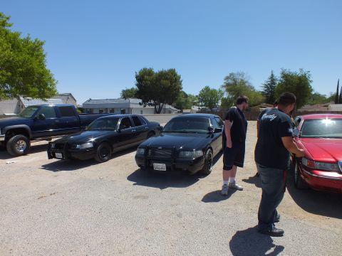 2003 Ford Crown Victoria - Two black Crown Victorias with grille guards as men inspect a red sedan nearby.