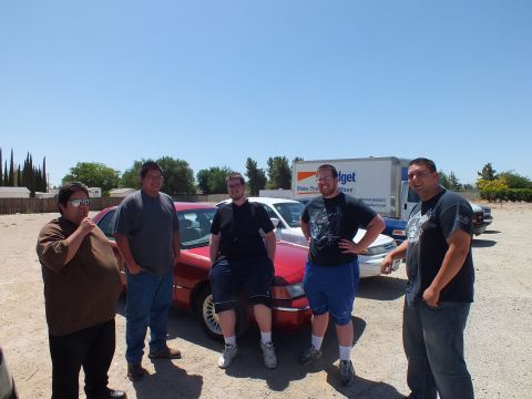 2003 Ford Crown Victoria - Five attendees pose leaning against a red Grand Marquis with a Budget truck behind.