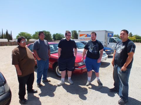 2003 Ford Crown Victoria - Group of five poses before a red full-size sedan with rental truck in background.