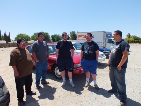 2003 Ford Crown Victoria - Five attendees gather in front of a red full-size sedan at a gravel-lot meet.