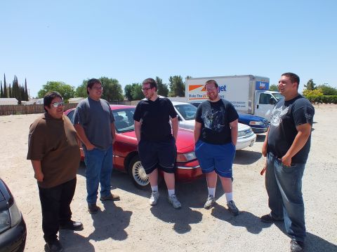 2003 Ford Crown Victoria - Attendees converse beside a red Grand Marquis with chrome wheels in the lot.