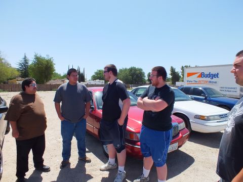 2003 Ford Crown Victoria - Group chats next to a red sedan with white and blue Crown Victorias parked behind.