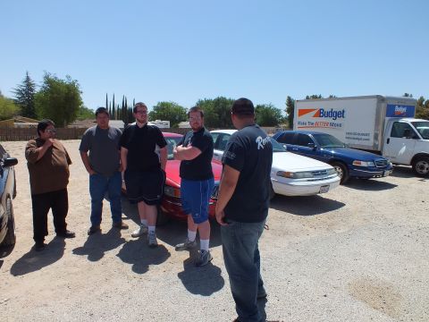 2003 Ford Crown Victoria - Attendees stand around a red full-size sedan with a Budget rental truck behind.