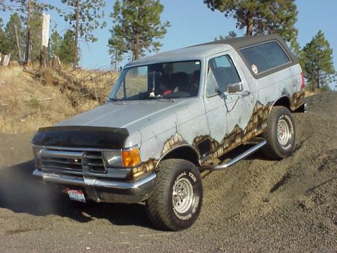 1989 Ford Bronco - Silver-gray full-size Ford Bronco with a black removable hardtop, photographed from the driver's-side front three-quarter angle while parke…