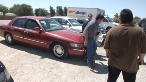 2003 Ford Crown Victoria - Dark red Grand Marquis parked next to a Budget box truck while men talk in a dirt lot