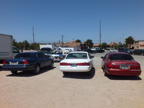 2003 Ford Crown Victoria - Three Panther-platform sedans in blue, silver and dark red parked rear-first on dirt
