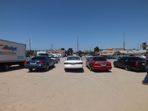 2003 Ford Crown Victoria - Lineup of dark and light full-size sedans beside a Budget box truck on open dirt lot