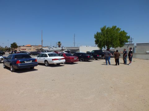2003 Ford Crown Victoria - Lineup of sedans along a dirt lot as several people gather near a tree on the right