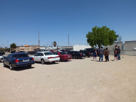 2003 Ford Crown Victoria - Multiple sedans lined up on dirt while a small group of people talks near a tree