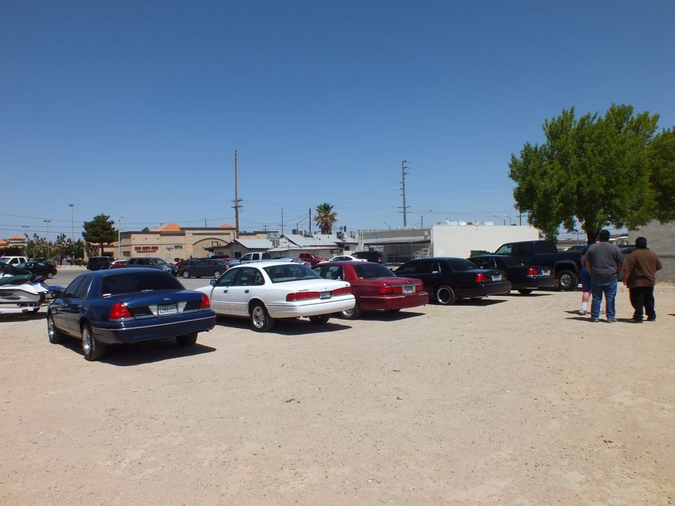 Row of full-size sedans and pickups parked diagonally across dirt lot