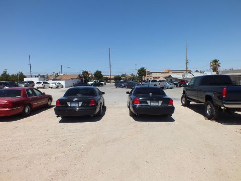 2003 Ford Crown Victoria - Two black sedans centered between a maroon sedan and a lifted pickup on dirt lot