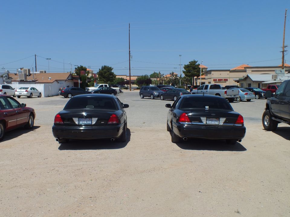 Two black full-size sedans parked rear-on with maroon car and pickup at edges