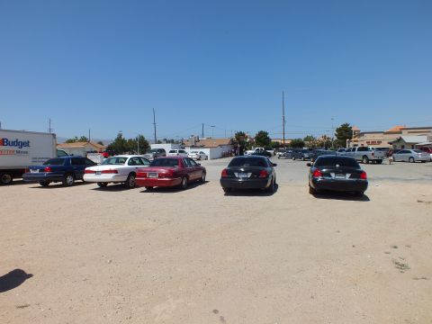 2003 Ford Crown Victoria - Full-size sedans and a black BMW parked across a dirt lot near a Budget truck