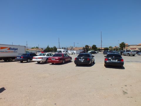 2003 Ford Crown Victoria - Blue, silver, maroon and black sedans angled across a dirt lot under clear sky