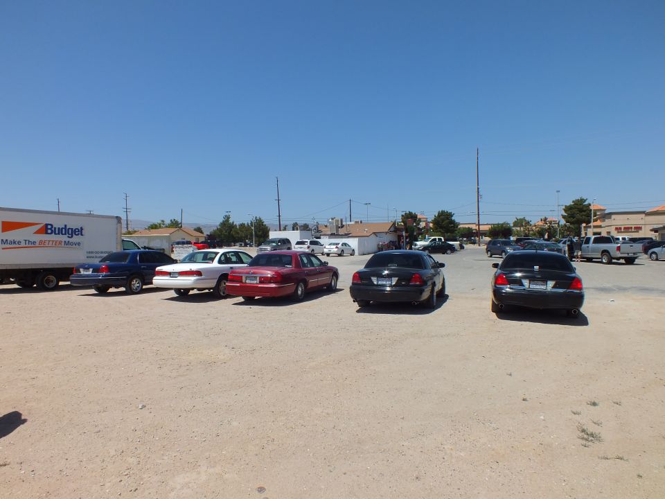 Lineup of full-size sedans and a BMW parked diagonally across open dirt lot