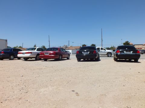 2003 Ford Crown Victoria - Blue, white, maroon, black and green full-size sedans parked rear-first on dirt