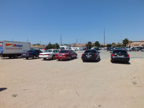 2003 Ford Crown Victoria - Several large American sedans line up on a gravel lot, a Budget moving truck at left under clear desert sky