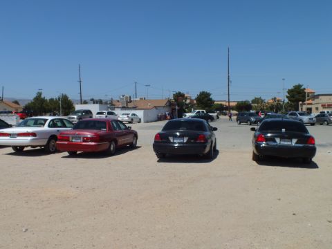 2003 Ford Crown Victoria - White, maroon and two black sedans sit in a bare lot, low buildings and power lines on the horizon