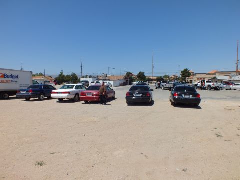 2003 Ford Crown Victoria - People gather among parked full-size sedans on a gravel lot, a Budget rental truck behind them