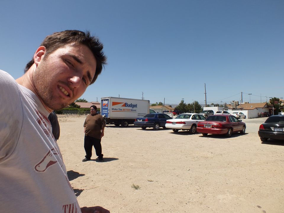 Man taking selfie in dirt lot with Budget truck and parked cars behind