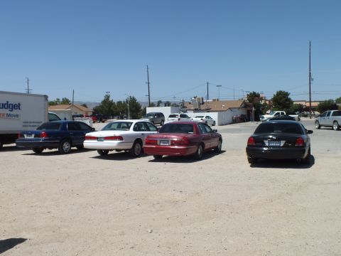 2003 Ford Crown Victoria - Four full-size sedans staged rear-out on a dusty lot with buildings and power lines behind