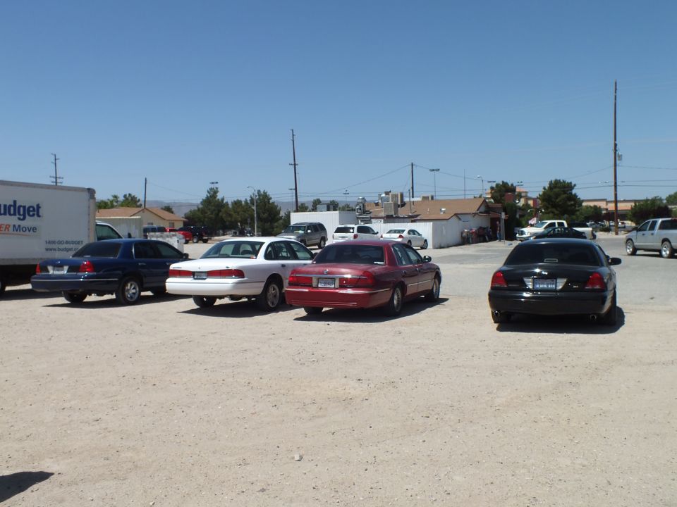 Blue, white, maroon and black sedans parked on gravel lot