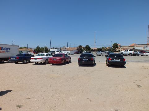 2003 Ford Crown Victoria - Blue, white, red and black sedans on bare ground under clear sky, businesses across the road