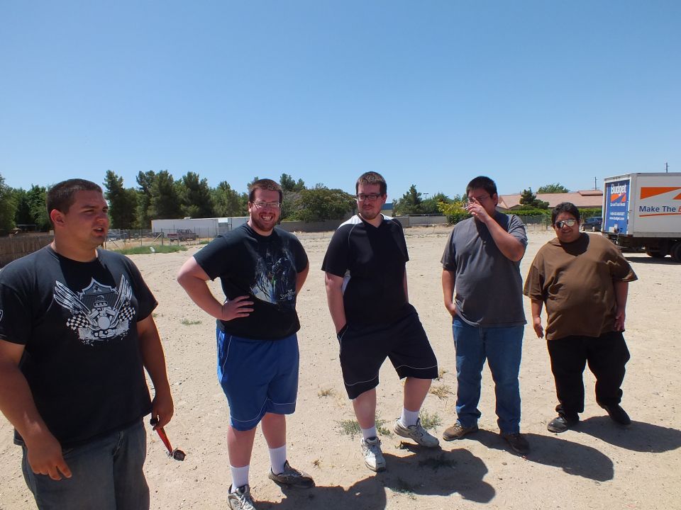 Five men standing in a row on dirt lot with rental truck behind