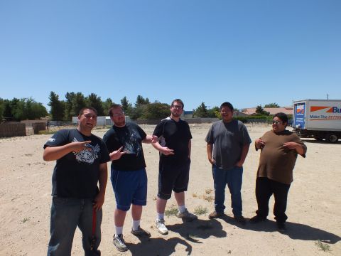 2003 Ford Crown Victoria - group of men make hand signs on a sandy lot, a Budget box truck and trees behind them
