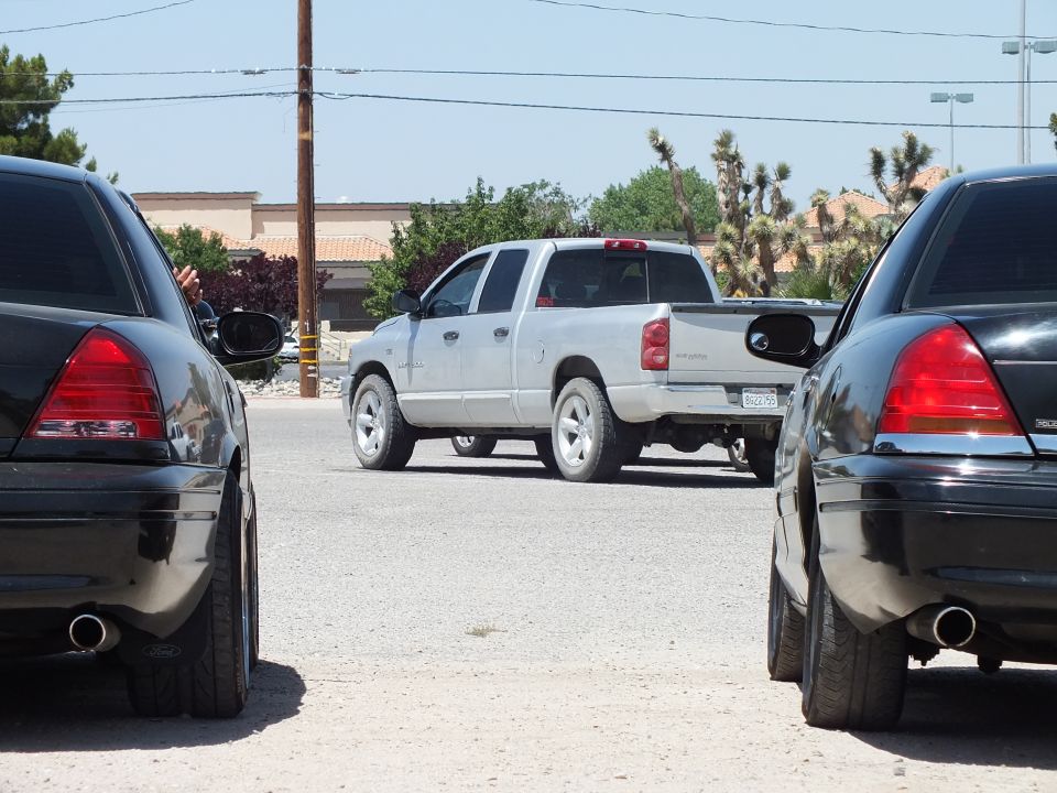 Two black sedan tails framing silver Dodge Ram pickup near Joshua trees