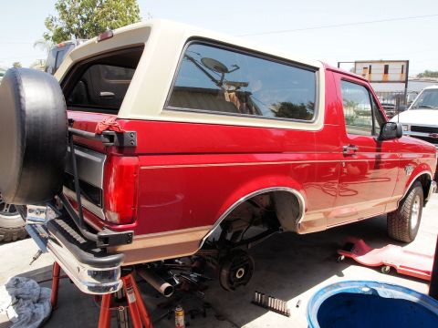 1994 Ford Bronco - Rear view of a red and tan 1994 Ford Bronco, showing its spare tire carrier and body style.