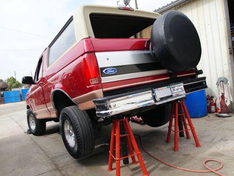 1994 Ford Bronco - Rear view of a red and tan Ford Bronco, supported by red jack stands in a workshop.